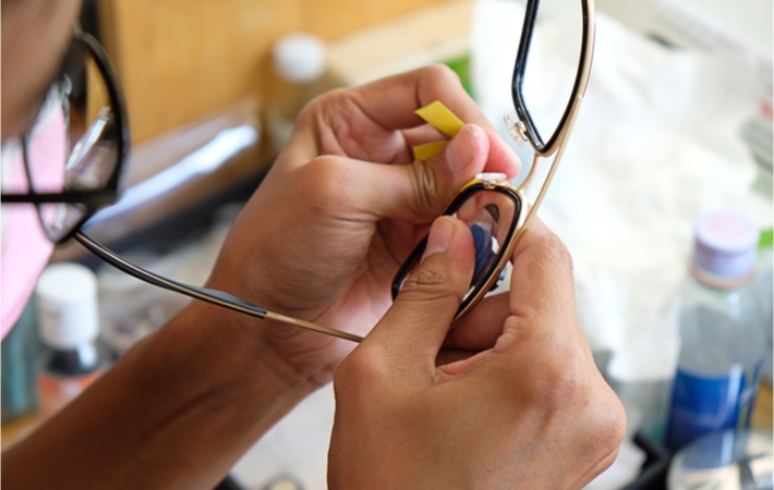 Close up view of an optician fixing a pair of glasses at a work desk.