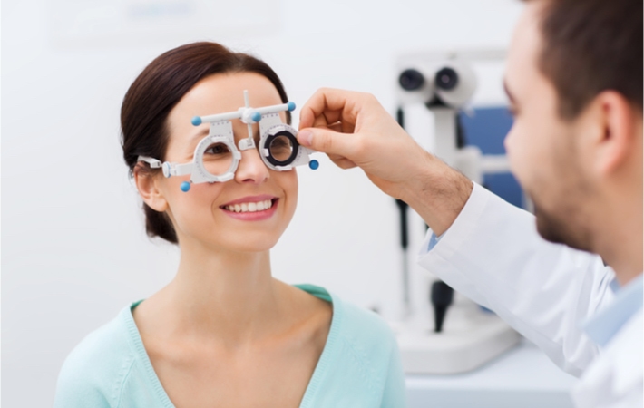 Image of a smiling female patient wearing a pair of trial frames that are being adjusted by the male optometrist.