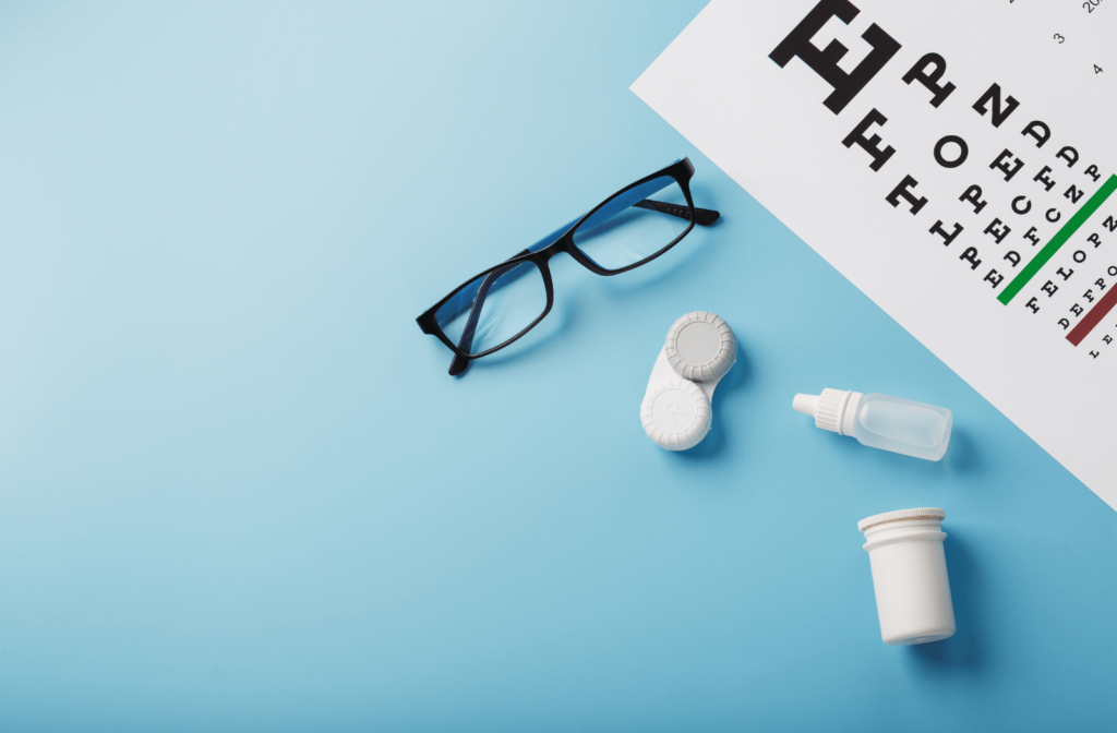 A pair of glasses, a contact lens case, contact lens solution and a Snellen eye chart sitting next to each other against a blue background