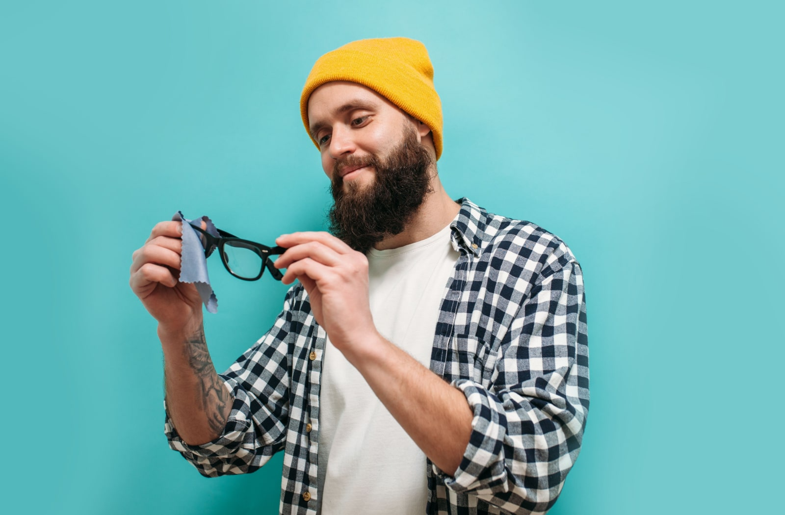 A man holding his pair of glasses while cleaning them with a microfiber cloth.