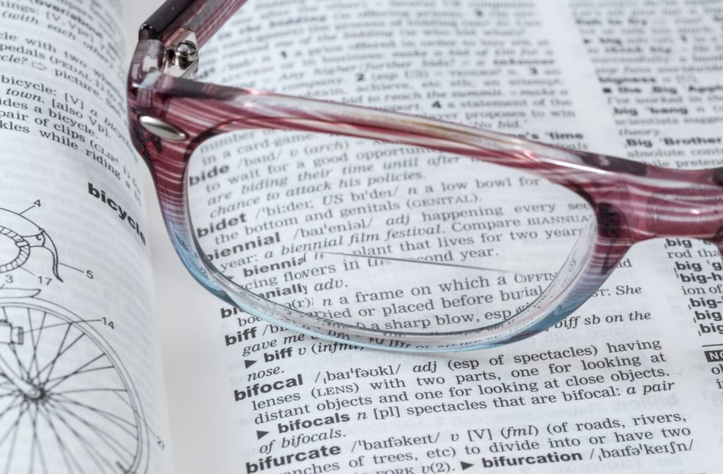 A pair of bifocal glasses sitting on a dictionary, with the word 'bifocal' under the glasses.