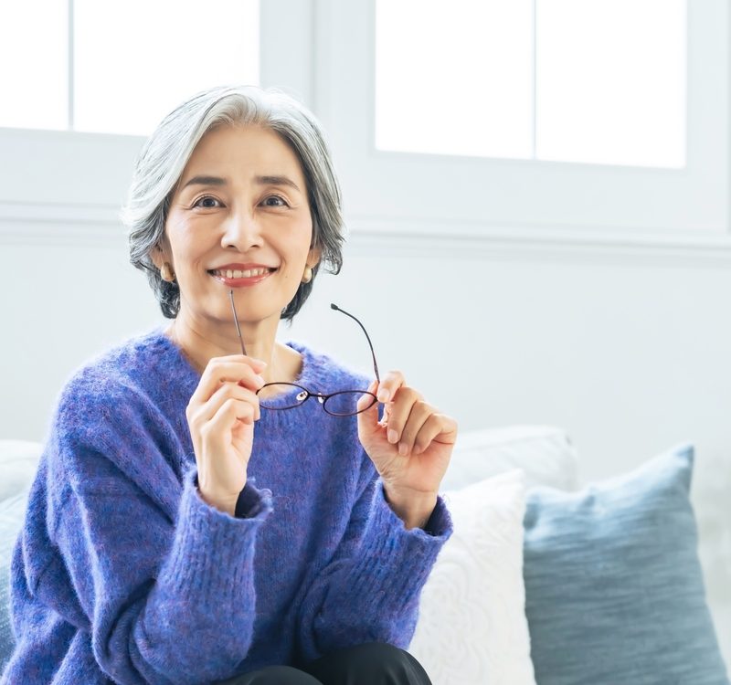 Smiling woman holding her eyeglasses indoors, representing everyday use and benefits of multifocal eyewear - whats progressive lenses