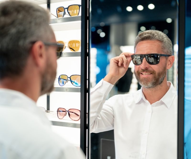 Man wearing polarized sunglasses while looking in a mirror at an eyewear store, demonstrating reduced glare and enhanced visibility benefits - polarized lenses for driving