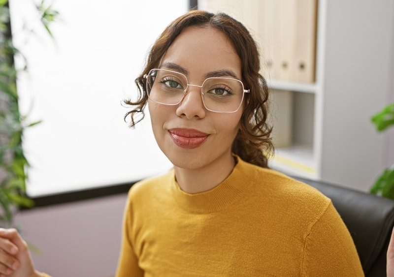 Woman wearing clear-frame eyeglasses in an office setting, representing eyewear maintenance and frame repair needs - replacement screw for glasses