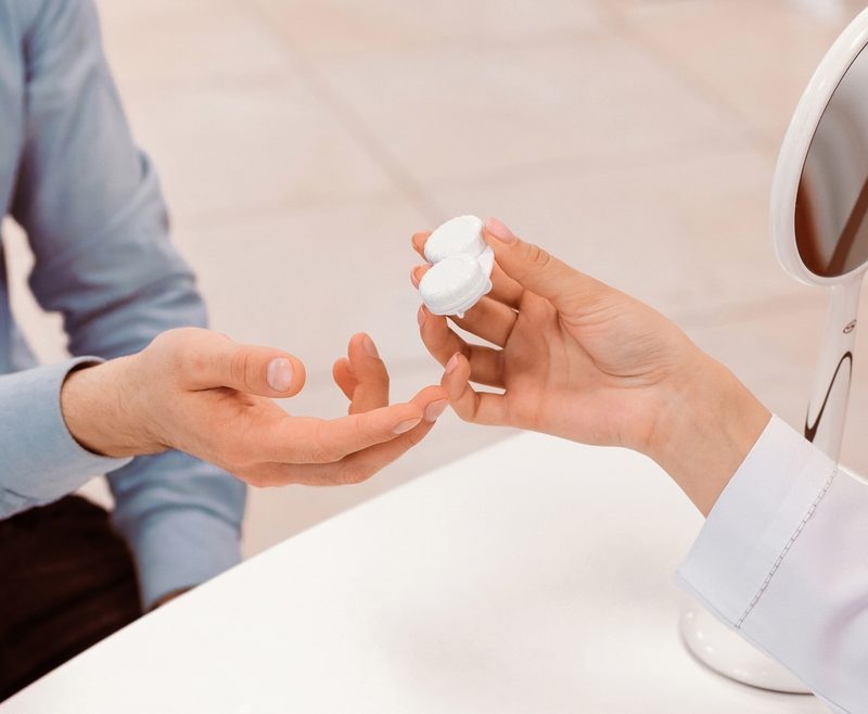 Eye care professional handing contact lenses to a patient during an eye exam while discussing differences between contact lens and eyeglass prescriptions - are contact lenses the same prescription to glasses