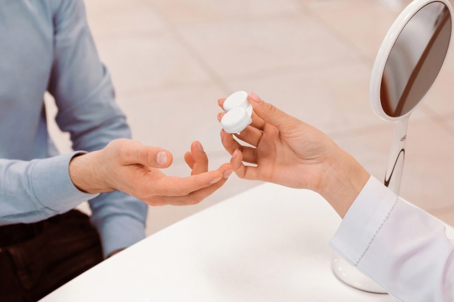Eye care professional handing contact lenses to a patient during an eye exam while discussing differences between contact lens and eyeglass prescriptions - are contact lenses the same prescription to glasses