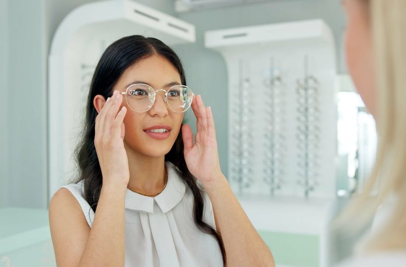 Woman adjusting her new eyeglasses in front of a mirror to ensure proper fit, alignment, and visual comfort - how to adjust new glasses