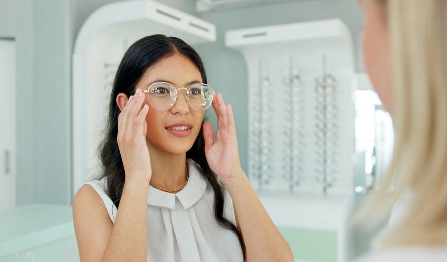 Woman adjusting her new eyeglasses in front of a mirror to ensure proper fit, alignment, and visual comfort - how to adjust new glasses