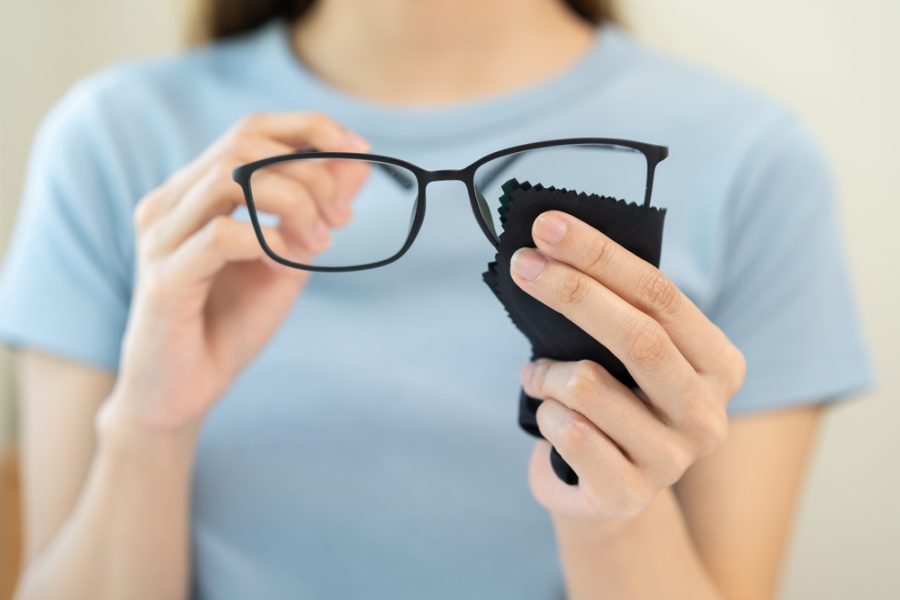 Person holding eyeglasses and a microfiber cloth while cleaning lenses with spray solution - glass cleaner on glasses